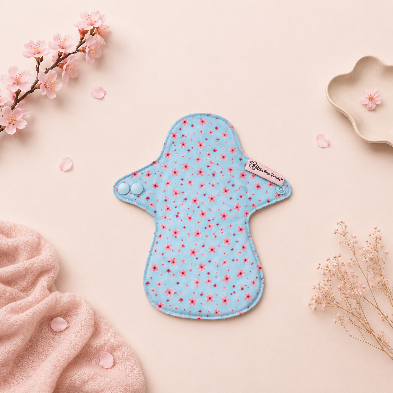 Blue floral-patterned cloth pad on a pink background with flowers and fabric.